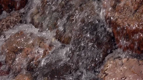 Slow motion of rapid water, falling and splashing over brown and red boulders. Stock Footage 90217588