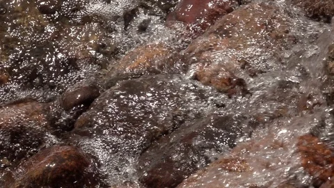 Slow motion of rapid water, falling and splashing over brown and red boulders. Stock Footage 90565805