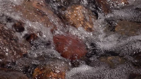 Slow motion of rapid water, running down over brown and red boulders. Stock Footage 90565601