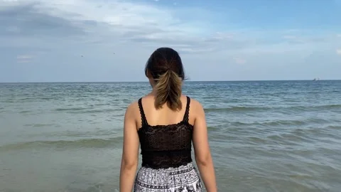 Slow motion rear view of young asian female walking towards ocean beach Stock Footage 255783259