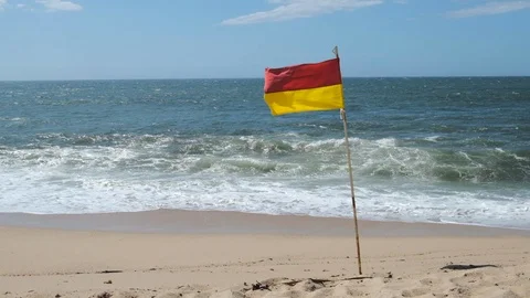 Slow motion red and yellow flag on beach, blowing in breeze. Wide shot. Stock Footage 115759480