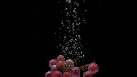 Slow motion red grapes falling into transparent water on black background Stock Footage 205190236