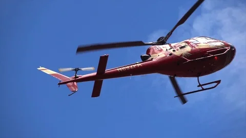 Slow motion red helicopter flies close up over head against a bright blue sky Stock Footage 97151704
