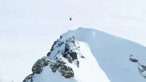 Slow motion of rescue helicopter flying above snowy mountain peaks on sunny day Stock Footage 129111104