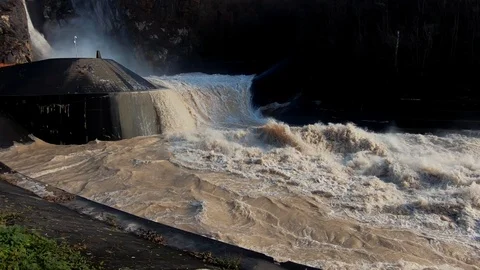 Slow motion right pan dirty brown turbulent flood water leaving dam Stock Footage 121679288