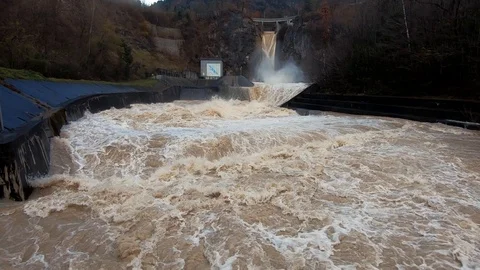 Slow motion right pan dirty brown raging turbulent flood water leaving dam Stock Footage 122205396