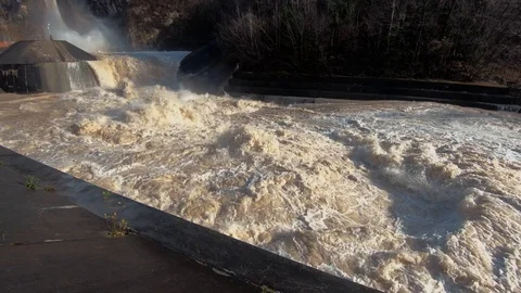 Slow motion right pan flood water leaving dam and spills in river canal Stock Footage 121679723