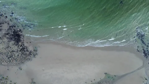 Slow motion rising drone shot of waves crashing along rugged sandy coastline at 스톡 동영상 332629693