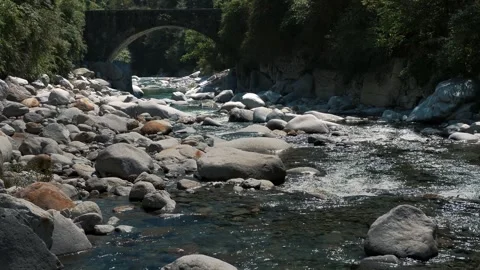 Slow motion of river near arched bridge among white boulders and green slopes Stock Footage 346186542