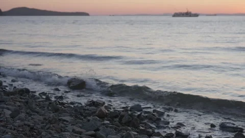 Slow-Motion Rocky Pebble Shore with Out-of-Focus Cruise Ship at Dusk in Stock Footage 344231658