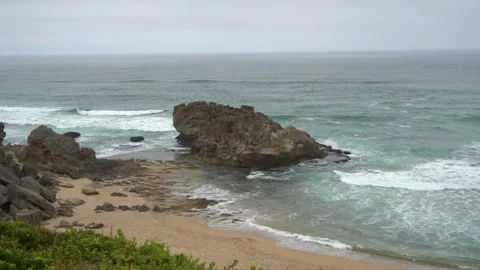 Slow motion rolling waves with a big beach boulder on a cloudy day Stock Footage 301510046