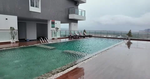 Slow-motion: rooftop pool, wet deck, and lounge chairs overlooking a misty sky Stock Footage 339389151