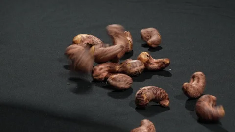 Slow Motion Salt-Roasted Cashew Nuts with Skin Falling on Black. Видео 333674948