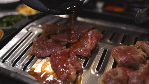 Slow motion sauce being poured over korean bbq meats while they cook on a grill Stock Footage 112732987
