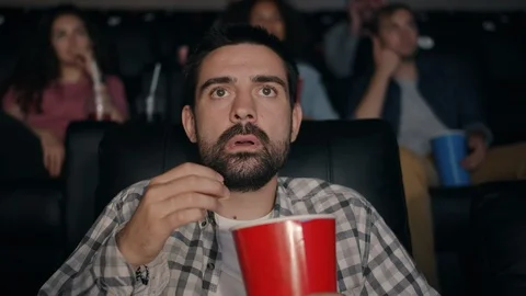 Slow motion of scared guy eating popcorn watching shocking movie in cinema Stock Footage 114979504