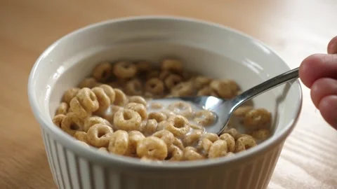Slow motion scooping honey cereal rings with a spoon from a bowl full of milk Stock Footage 294696904