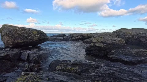 Slow motion sea waves making rock boulder pool under blue sky Stock Footage 325720814