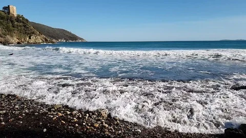 Slow Motion - Sea waves on a rocky lone beach with a tower in a sunny day Stock Footage 107880695