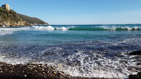 Slow Motion - Sea waves on a rocky lone beach with a tower in a sunny day Stock Footage 107880711