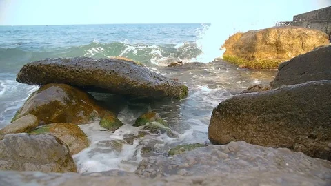 Slow motion sea waves splashing against rocks on blue sky Stock Footage 80653348