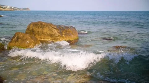 Slow motion sea waves splashing against rocks on blue sky Stock Footage 80654772