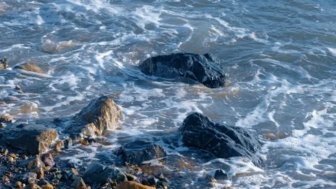 Slow motion sea waves with white foam washing up pebble stones and rocks on the Stock Footage 121533304