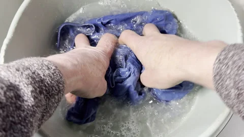 Slow motion of a senior man’s hands squeezing a blue shirt in soapy water. Stock Footage 300369705