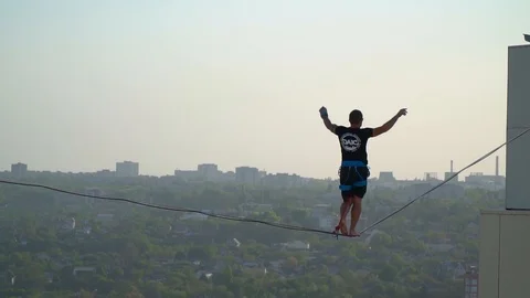 Slow motion shooting a man walking along a tight rope past birds fly by Stock Footage 90281641