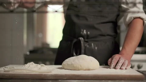 Slow motion shot: Baker pours flour on dough for bread. Baker sprinkles pinch of Stockbeeldmateriaal 138527870