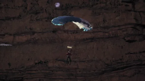 Slow motion shot of base jumper descending with open parachute. Stock Footage 52225877