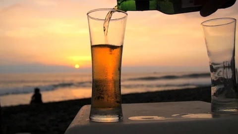 Slow motion shot of beer being poured into a glass on a beach Stock Footage 87857708