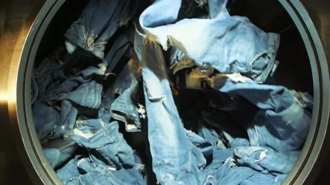 Slow motion shot of blue jeans spinning inside an industrial washer dryer Stock Footage