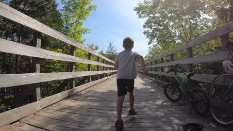 Slow motion shot of a boy running across a wooden bridge in the forrest Stock Footage 114107762