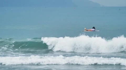Slow motion shot of breaking surf waves and a surfer floating in the blue sea. Stock Footage 154228416