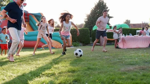 Slow Motion Shot Of Children Playing Football Match With Adults At Summer Garden Stock Footage 99743398