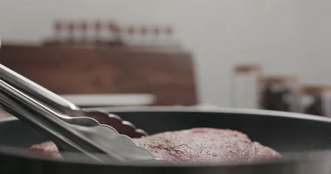 Slow motion shot of cooking new york steak on nonstick pan with tongs Stock Footage 148410053