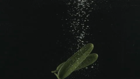 Slow Motion Shot of Cucumbers Falling into Water on black Background at. Stock Footage 171544722