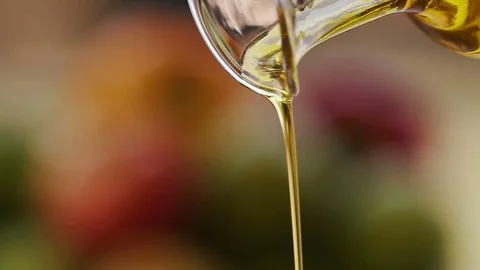 Slow motion shot of extra virgin olive oil being poured out a clear glass bottle Stock Footage 78196512