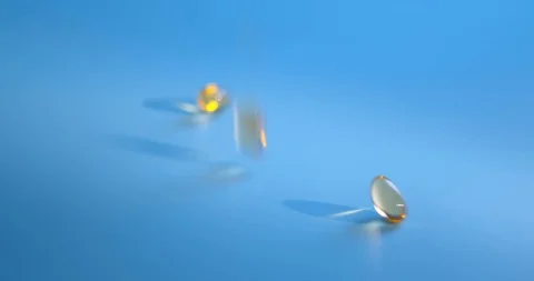 Slow motion shot of falling Omega 3 Fish Oil capsules on blue background. Golden Stock Footage 126106831