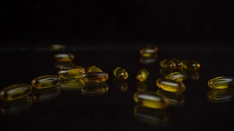 Slow motion shot of falling Omega 3 Fish Oil capsules on black mirror background Stock Footage 135582655