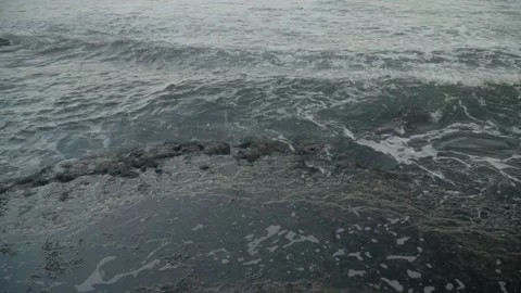 Slow motion shot of foams created by the ocean waves meet a rocky shoreline. Stock Footage 312861420