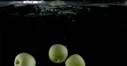 Slow-motion shot of a fresh green apple being thrown into water. Stock Footage 300487613