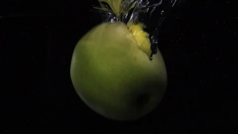 Slow motion shot: green apple falls and floats in water. Black background. Food Stock Footage 105608024