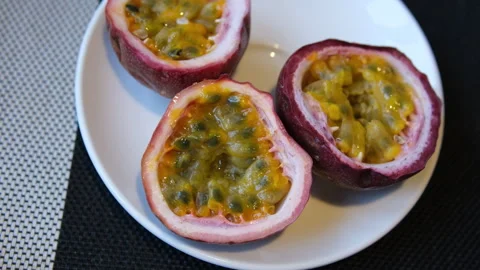 Slow motion shot of a hand taking a half cut passionfruit from the plate Video stock 310372459