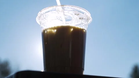 Slow motion shot of an iced coffee in front of the sun Stock Footage 130753049
