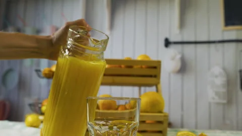Slow motion shot of juice from pitcher being poured into glass near orange Stock Footage 341248629