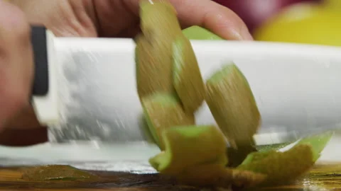 Slow motion shot of large knife cutting skin off kiwi on chopping board Stock Footage 341255177