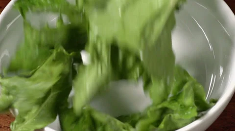 Slow motion shot of lettuce falling into a bowl on a wood table. Vídeo Stock 34663163