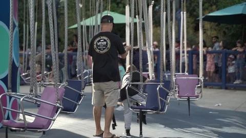 Slow motion shot of man and child getting on roller coaster in fun park Stock Footage 121756594