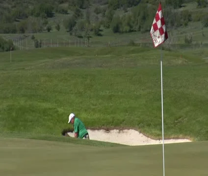 Slow-motion shot as  Man chips out of sand trap  to green with snowy mountains Stock Footage 21657719